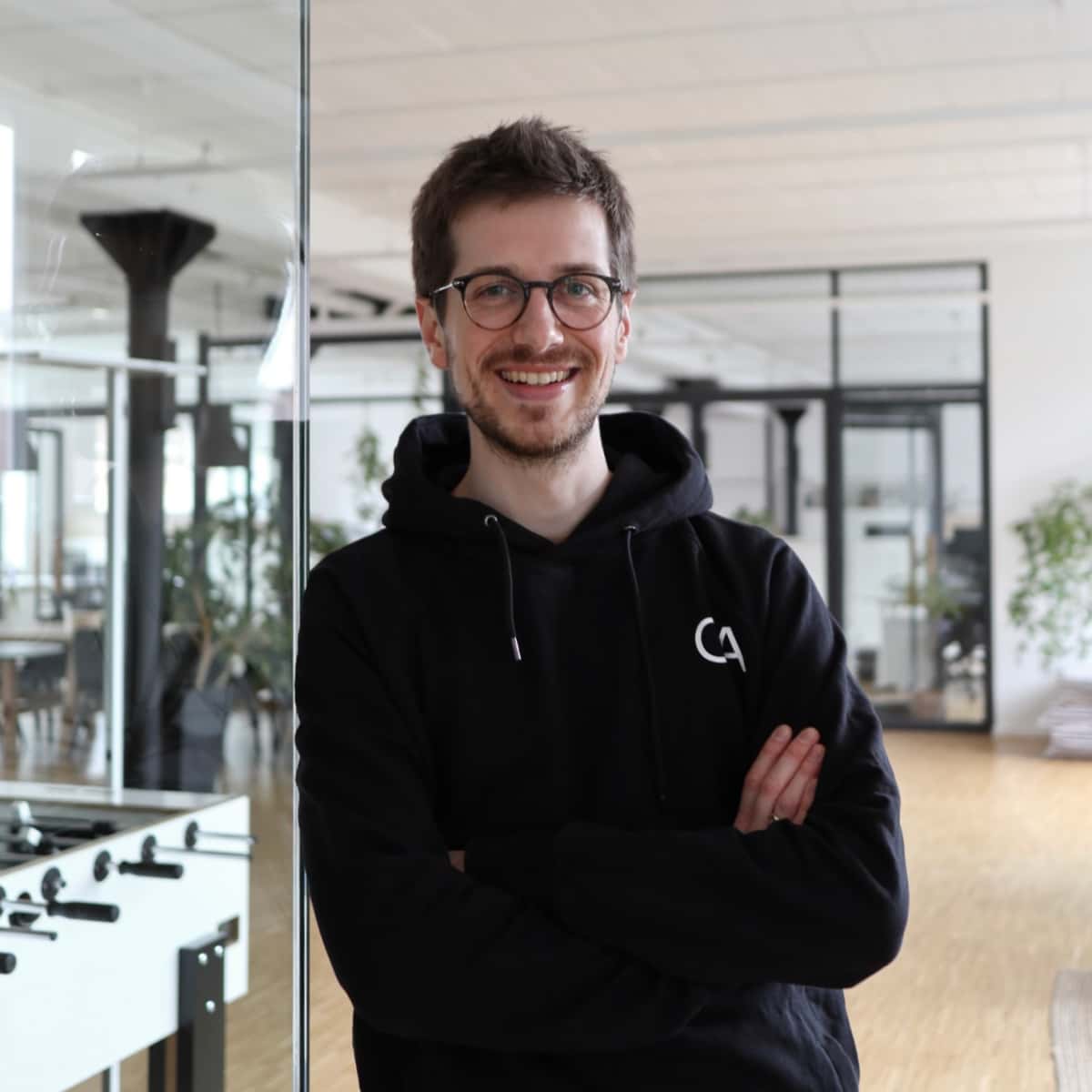 Timo Clasen steht angelehnt an einen gläsernen Konferenzraum im Codeatelier Büro und lächelt.